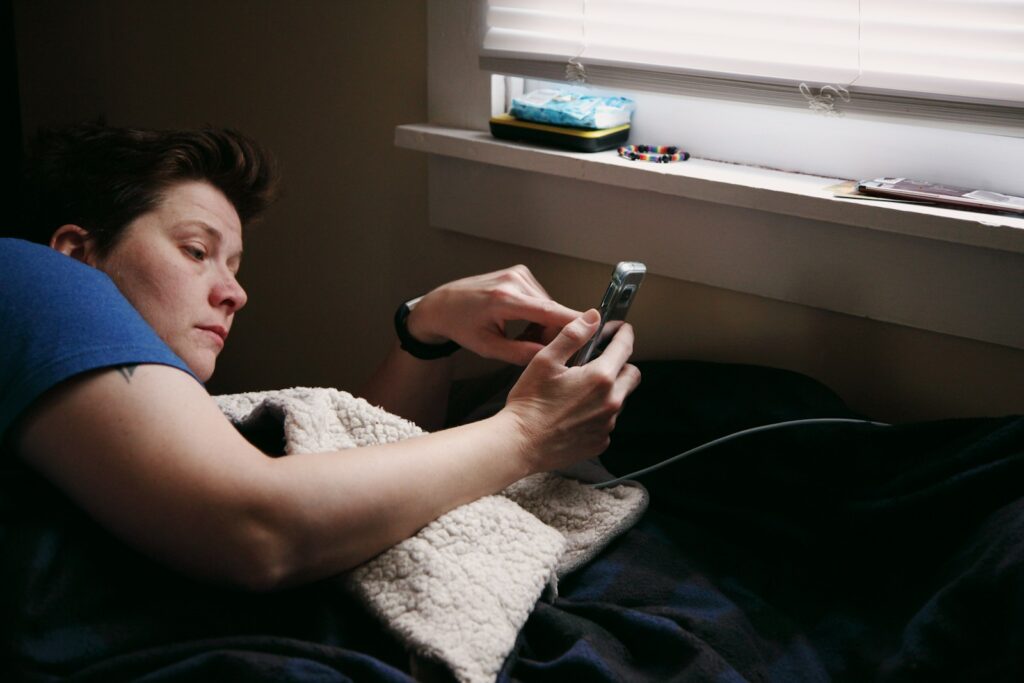 women in bed holding black smartphone